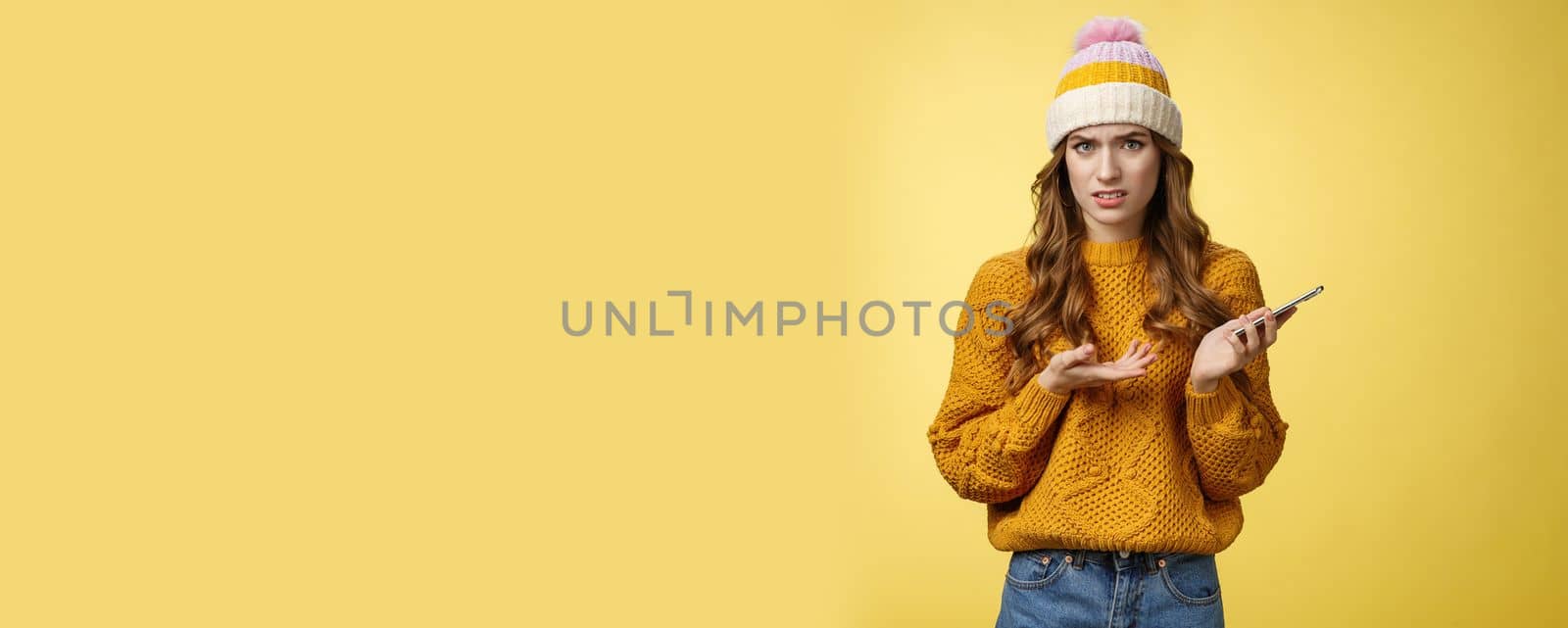 Confused cringing annoyed young woman shocked how friend talked her frowning raise hand dismay look frustrated camera holding smartphone finish video call unpleasant note, yellow background by Benzoix