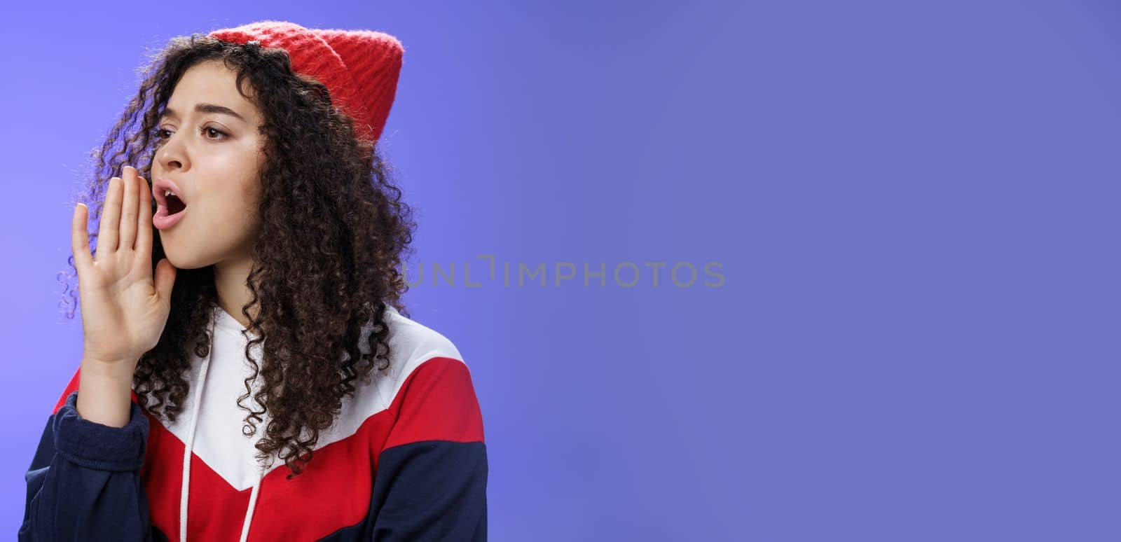 Portrait of worried sister calling sibling outdoors open mouth looking left seriously and holding palm near lips as shouting name searching someone, posing concerned over blue background by Benzoix