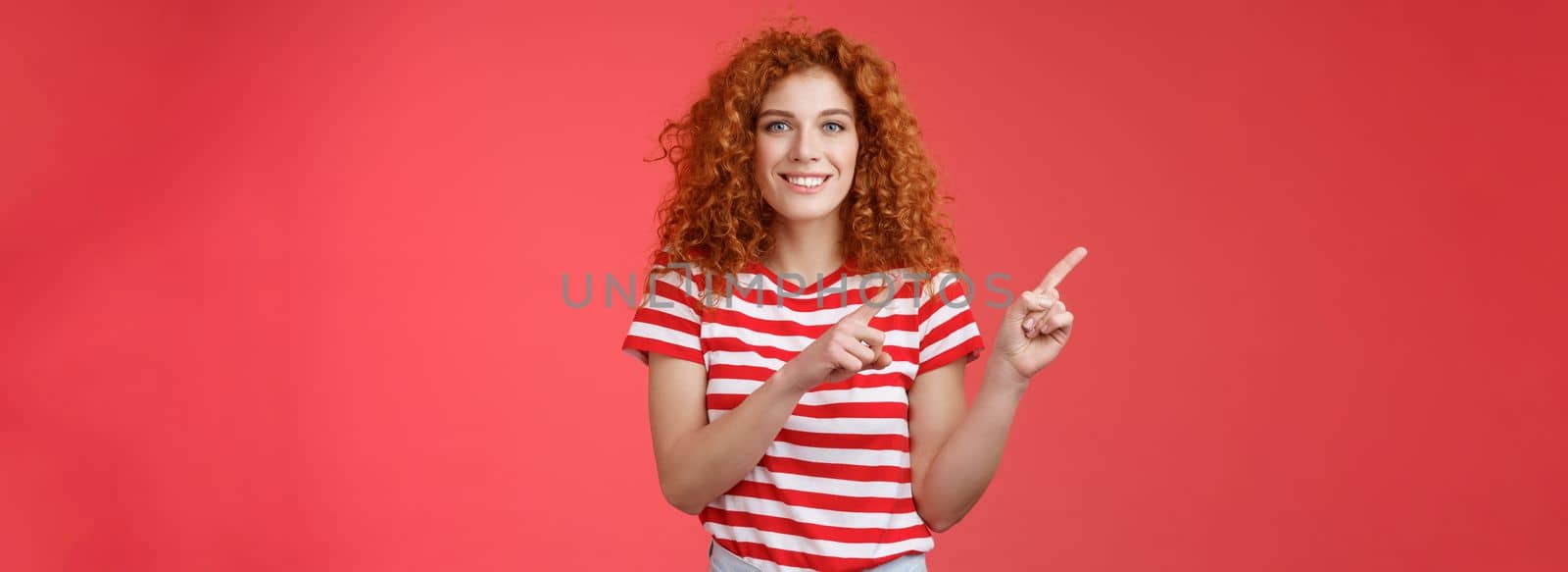 Joyful friendly attractive helpful cute redhead european female advice cool store promo pointing upper left corner blogger showing around perfect place spend summer holidays, red background.