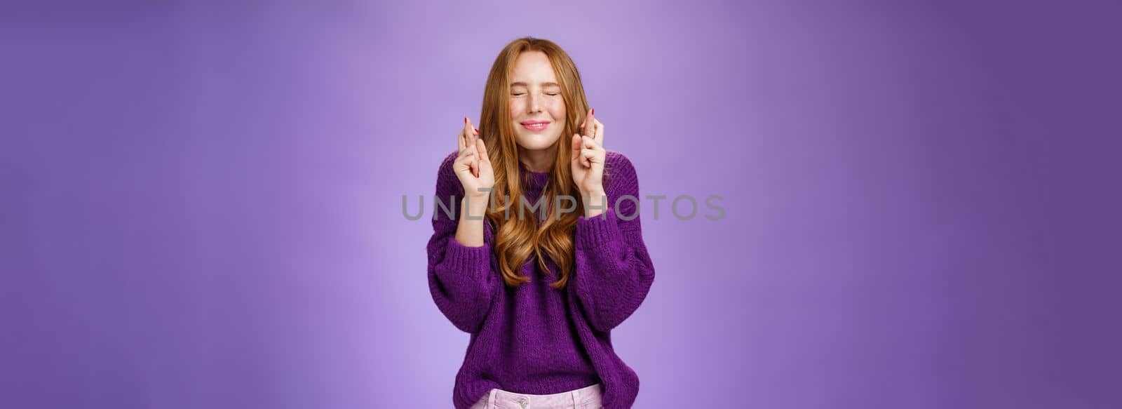 Girl makes wish eager dream come true. Atractive hopeful and positive young redhead woman in purple sweater close eyes and smiling as cross fingers for good luck, praying and anticipating miracle by Benzoix