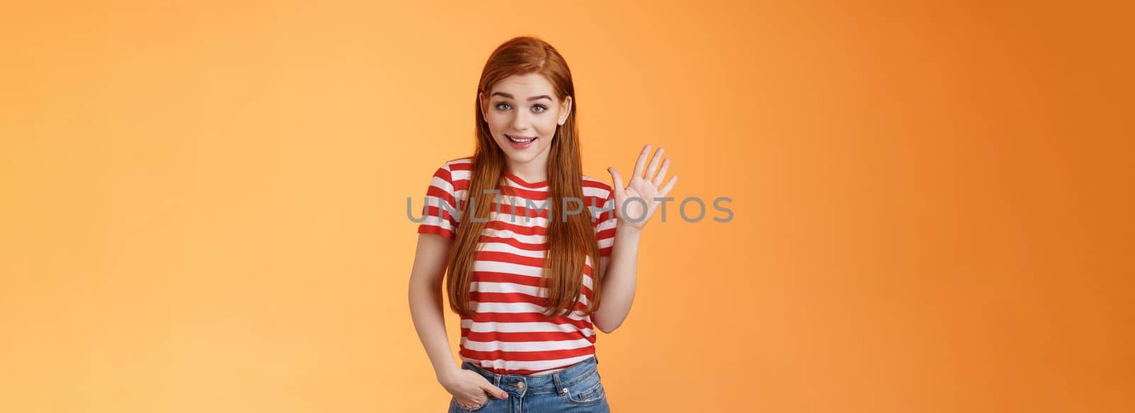 Hello how are you. Cute modest redhead newbie student female say hi, waving hand friendly, get know coworkers, smiling joyfully, introduce herself, welcome home, stand orange background.