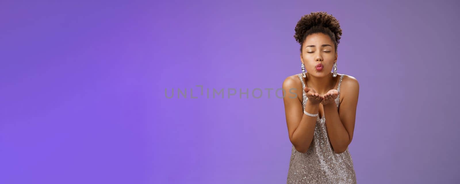 Charming lovely elegant african-american flirty girlfriend in glittering silver dress close eyes folding lips mwah hold hands near mouth send air kiss romantic expressing passion, blue background by Benzoix