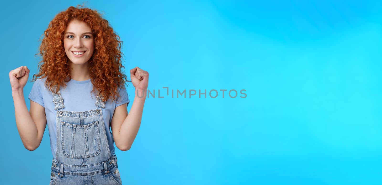 Motivated determined self-assured attractive redhead cheerful girl clench fists empowered woman assured everything gone well lucky summer day smiling delighted confident blue background.