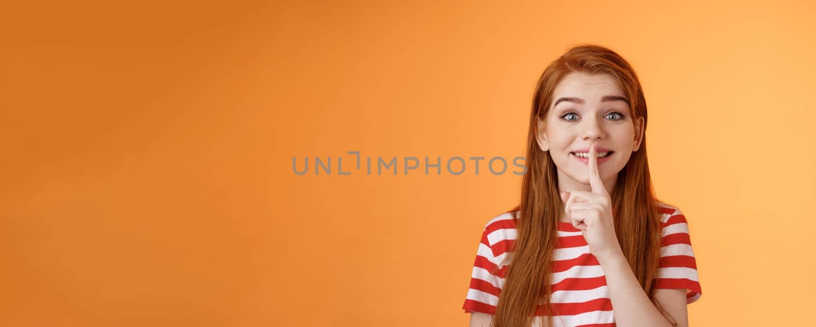 Close-up charming cute silly redhead girl making surprise party, taking promise from friends not tell anyone, smiling broadly positive grin, hush gesture, hold finger pressed lips shush, shh sign.