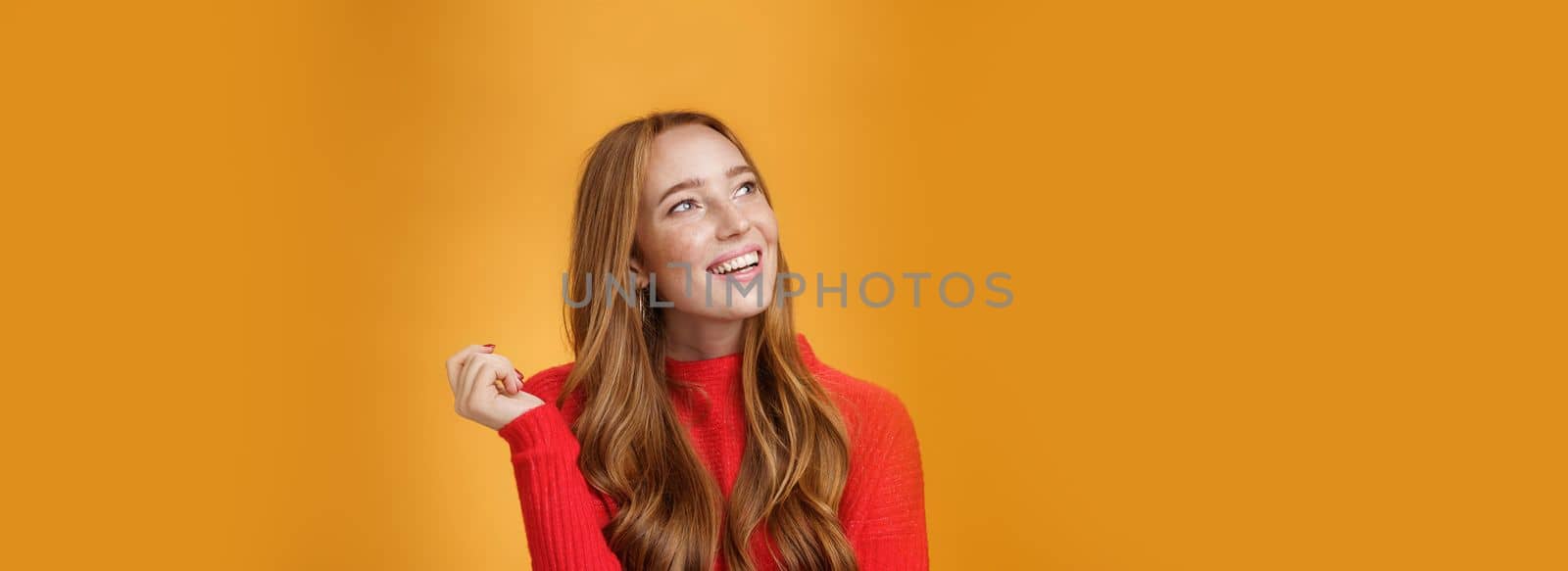 Close-up shot of nostalgic cute and sensual friendly-looking european female with nice cute memories looking at upper left corner dreamy and delighted, imaging and picturing desire over orange wall.