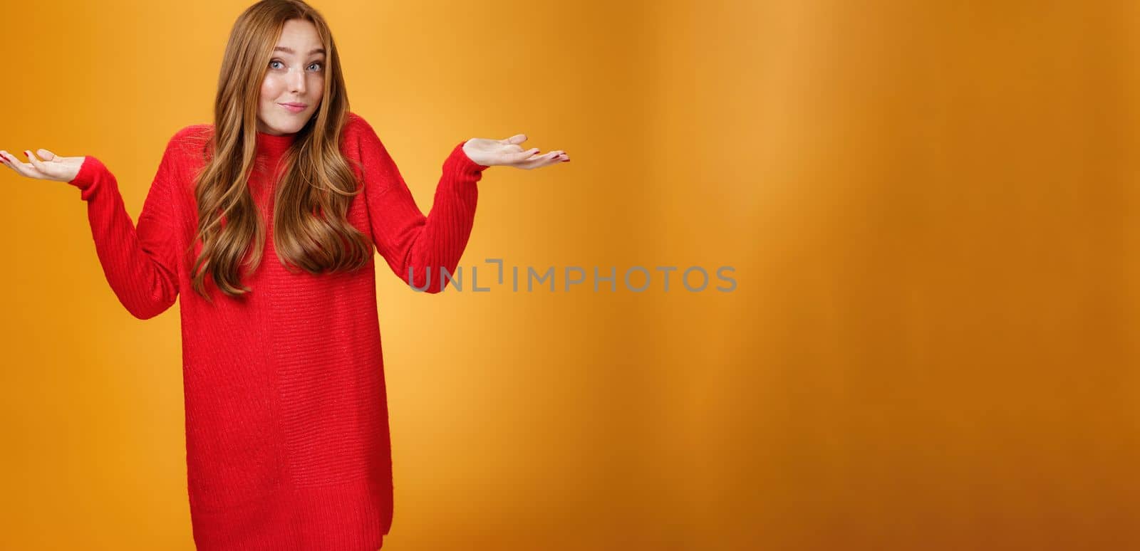 What do I know. Portrait of confused clueless tender and gentle redhead woman in red sweater shrugging with hands raised near shoulders turning away questioned and unaware, not knowing.