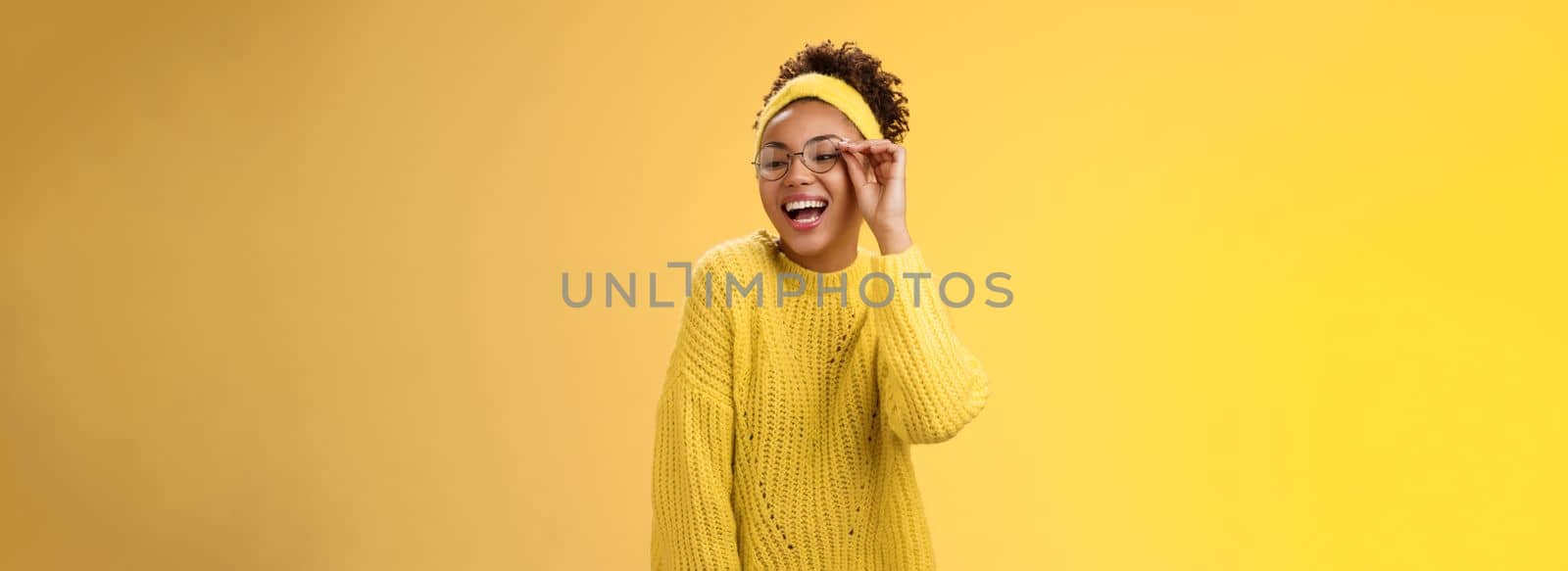 Charismatic stylish confident beautiful african-american joyful teenage girl touching glasses nose laughing broadly look down right corner grinning have fun joking enjoying, yellow background.