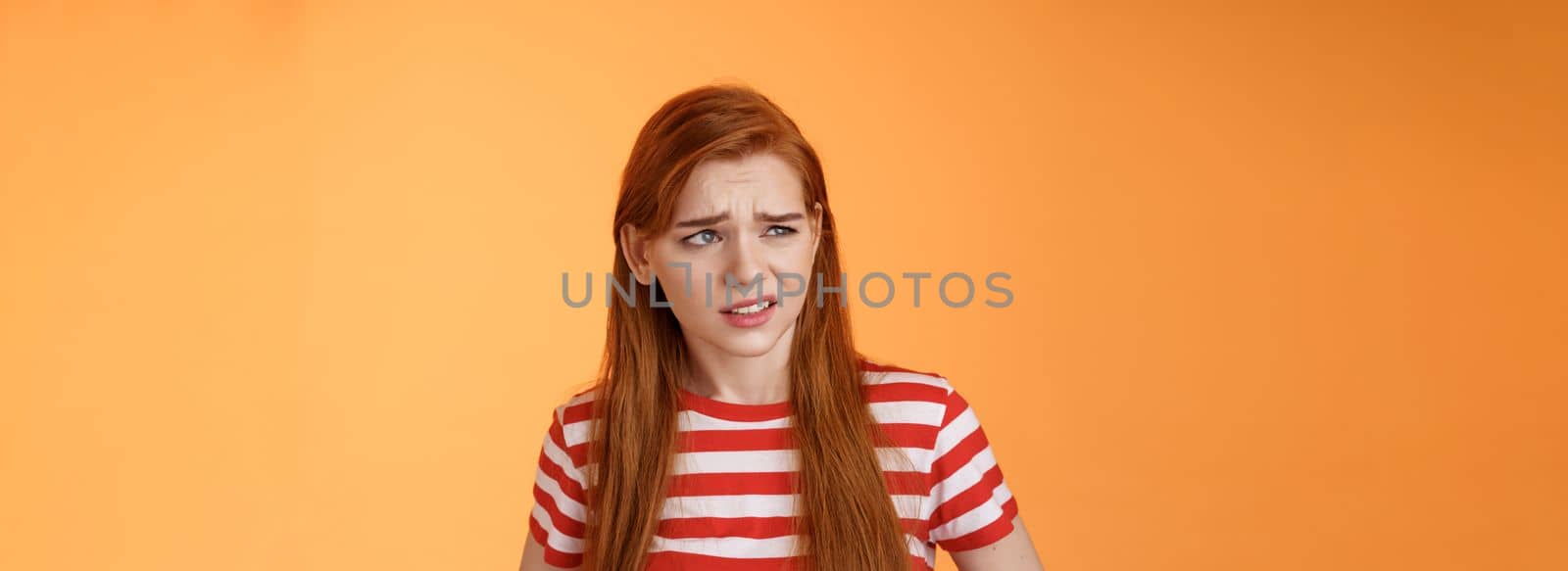 Close-up unsure redhead teenager frowning uncertain, having doubts, look perplexed left side copy space, hesitating, cringe dislike and disappointment, stare frustrated, uneasy decision by Benzoix