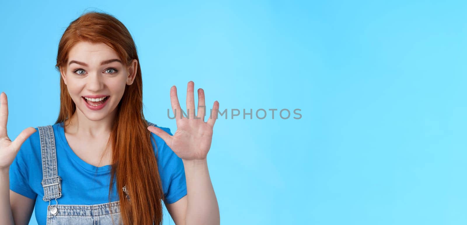 Close-up friendly joyful redhead caucasian girl, long ginger hairstyle, raise hands show number ten, counting dozer, explain fingers, raise arms surrender, smiling joyful, stand blue background.