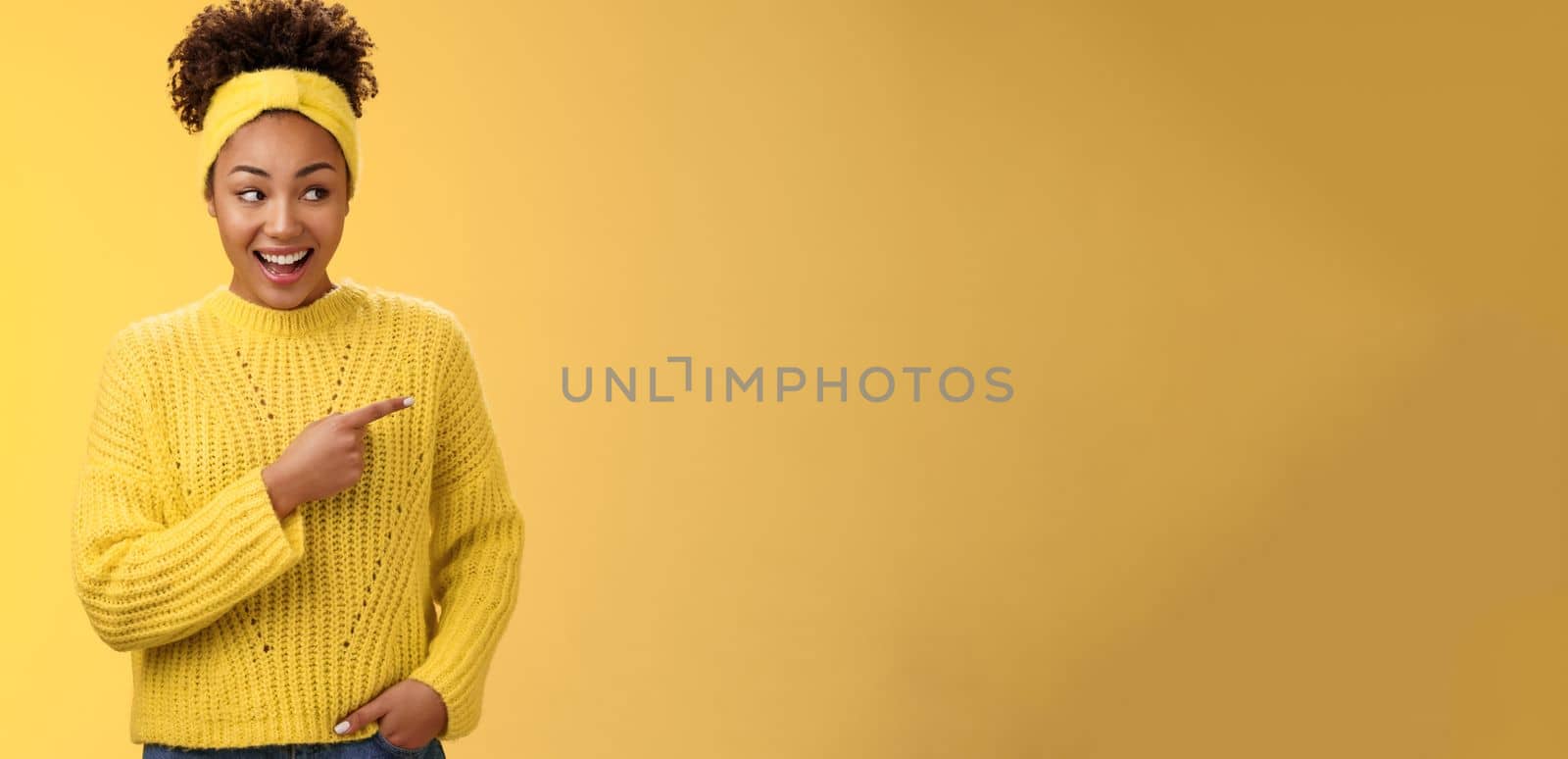 Astonished cute feminine modern african-american woman gossiping silly laughing drop jaw laughing surprised pointing right discuss during conversation interesting rumour place, yellow background.