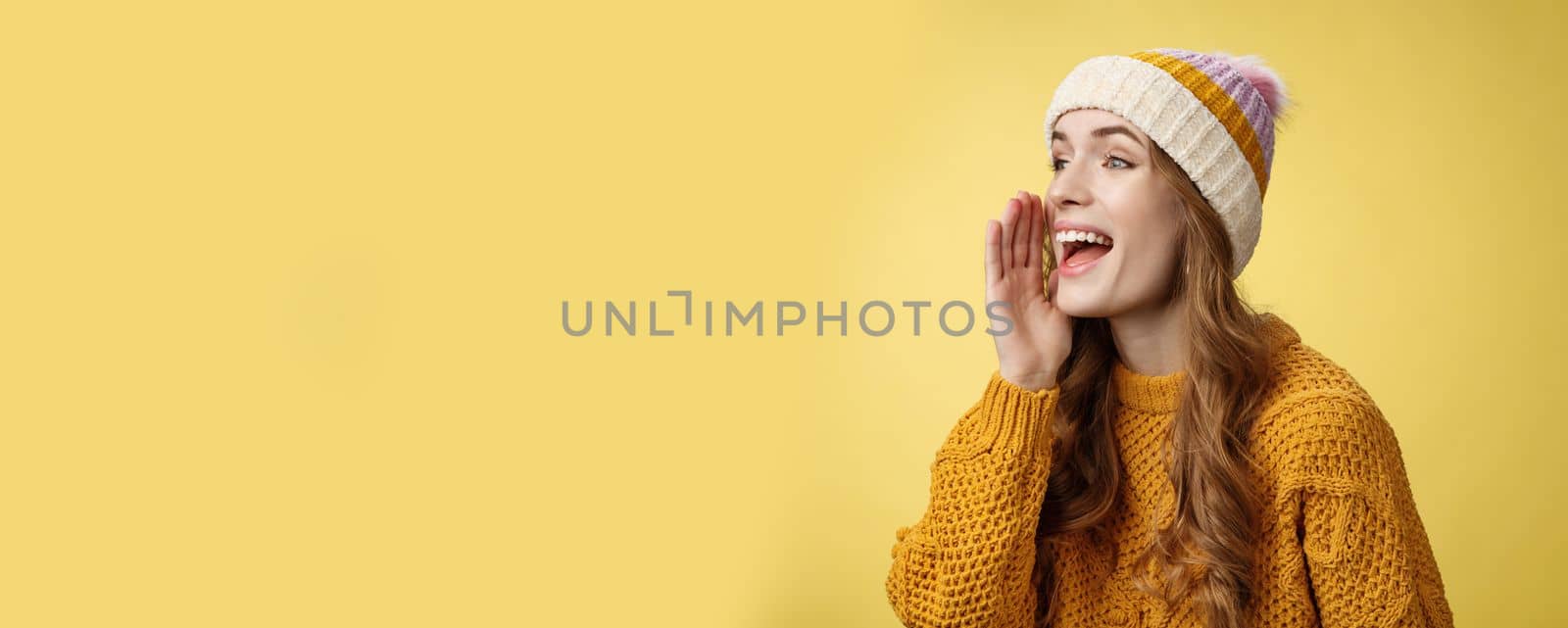 Attractive happy girlfriend shout call boyfriend standing far away take pic, turning left scream hold hand near opened mouth seek friend yelling loudly, search someone, yellow background.