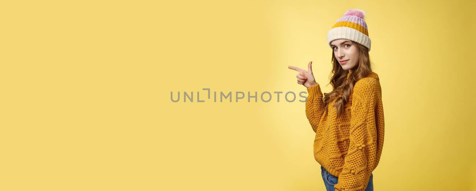 Profile shot confident flirty fashionable young 20s girl turning camera smiling pointing left inviting go together showing curious promotion cool place hang out, standing yellow background relaxed.