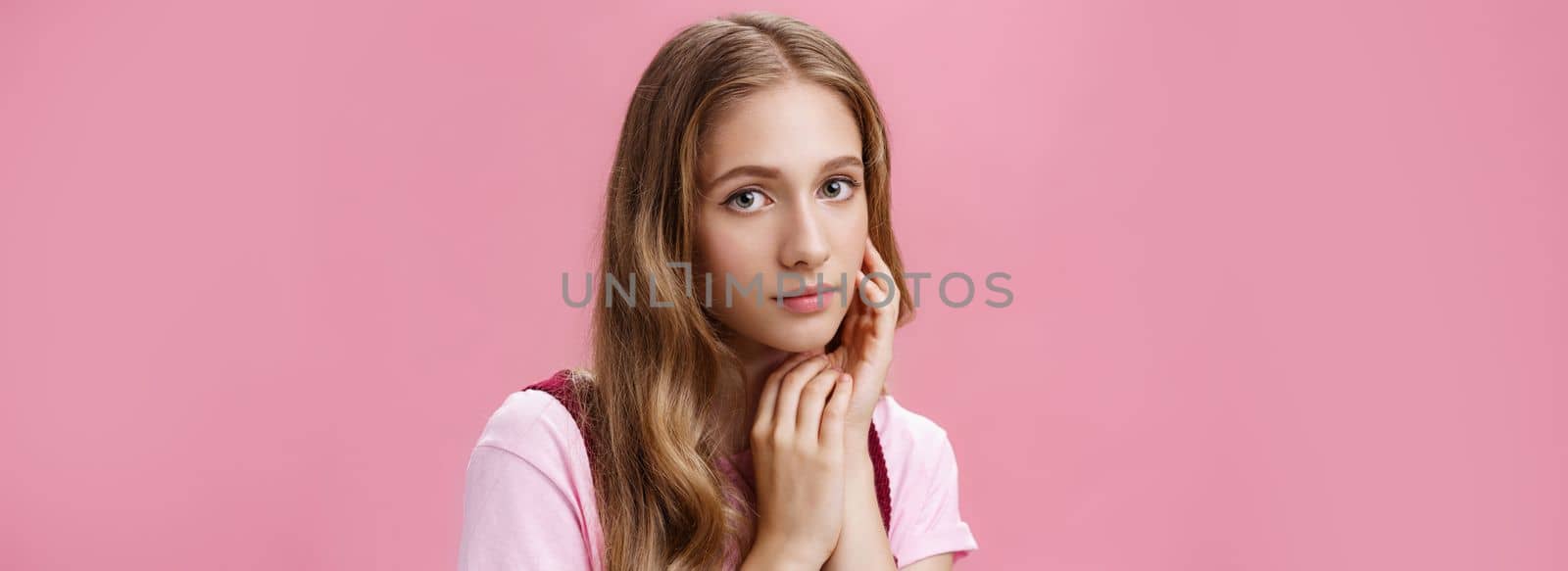 Woan feeling beautiful the way she is. Charming feminine and tender young girl with fair wavy natural hair and slight make-up touching face gently taking care of skin with organic cosmetics.