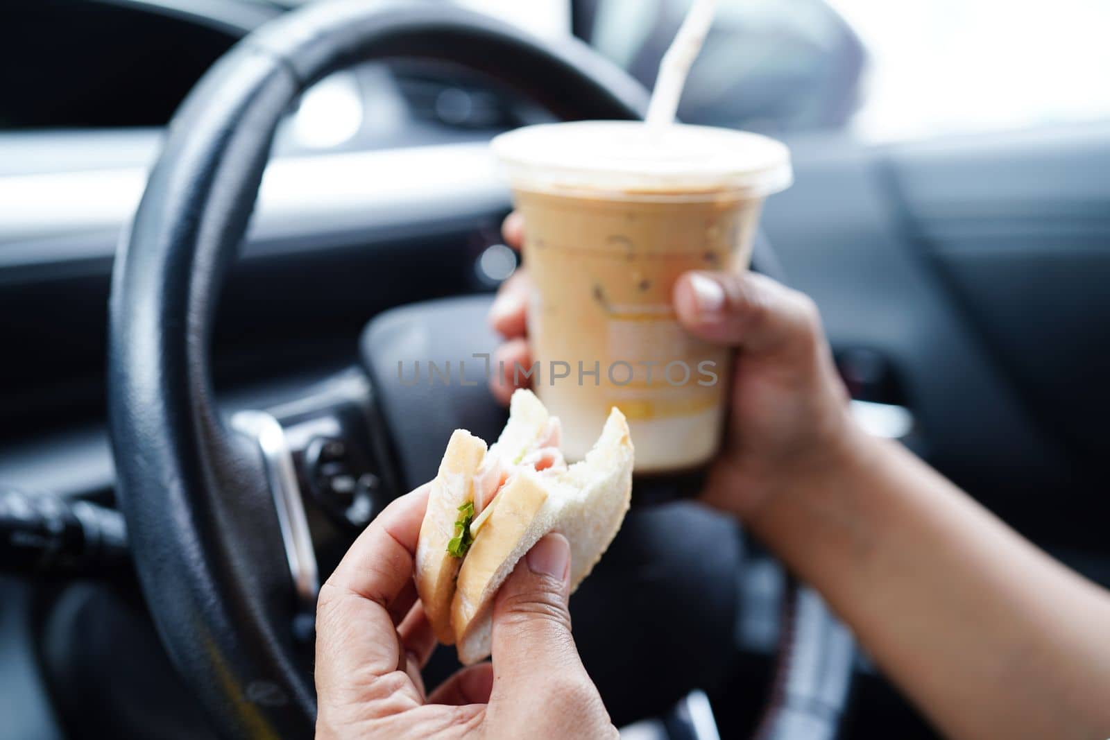Asian woman driver hold ice coffee cup and sandwich bread for eat and drink in car, dangerous and risk an accident. by sweettomato