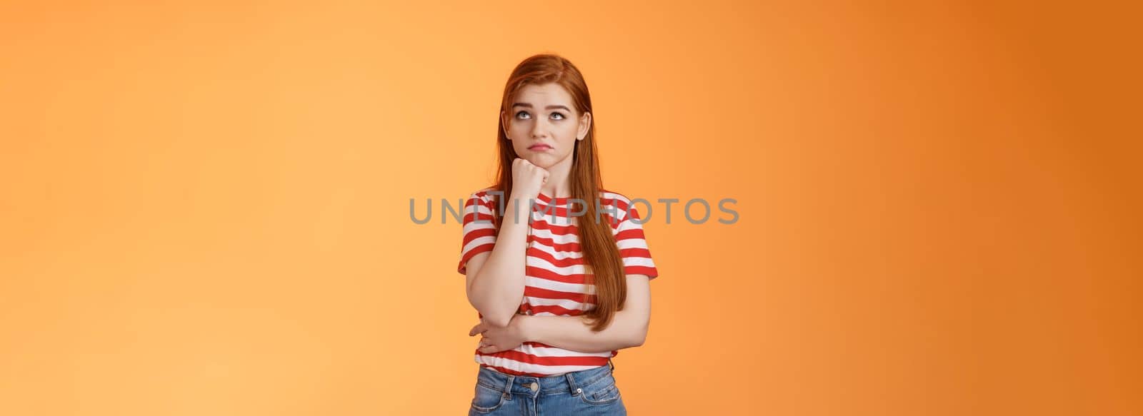 Upset redhead woman losing lottery feel uneasy distressed, look up regret loss, lean on fist pulling sad face, standing lonely unhappy orange background thinking, taking hard decision.