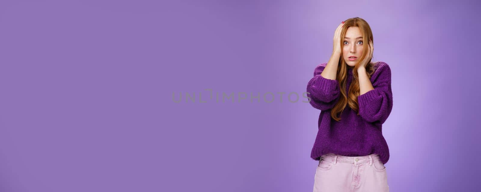 Girl in stupor feeling shocked and troubled as realising huge mistake made, holding hands on face and head popping eyes at camera confused and hopeless, posing anxious over purple background by Benzoix