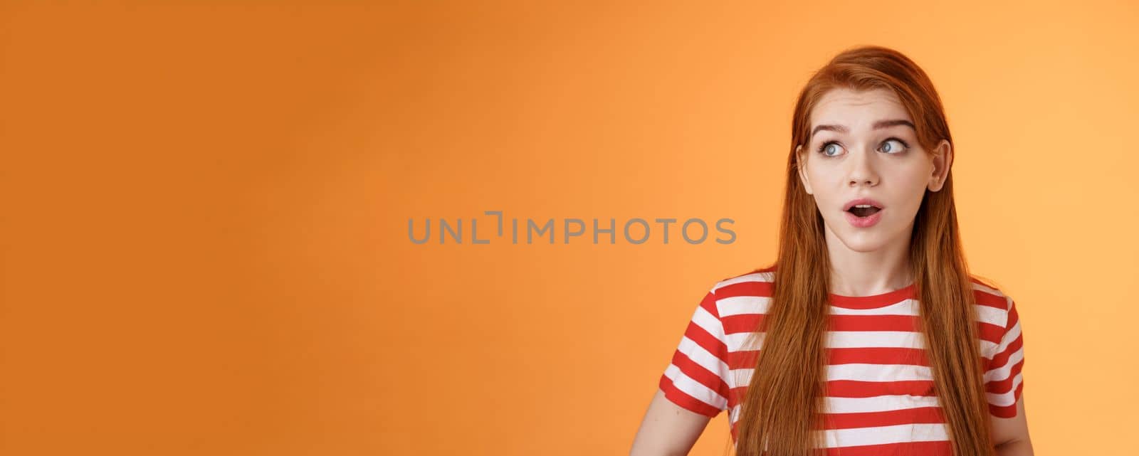 Close-up enthusiastic surprised, intrigued redhead caucasian woman look impressed left copy space, open mouth charmed amused, stare speechless, stunning cool promo, stand orange background.