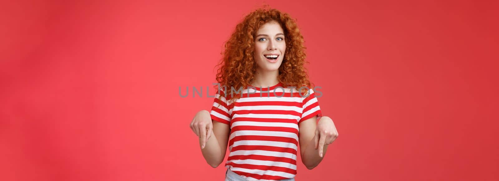 Hey check it out friend. Sassy good-looking cheeky redhead stylish girlfriend curly hairstyle wear summer t-shirt pointing down index finger smiling amused delighted present awesome recommendation.