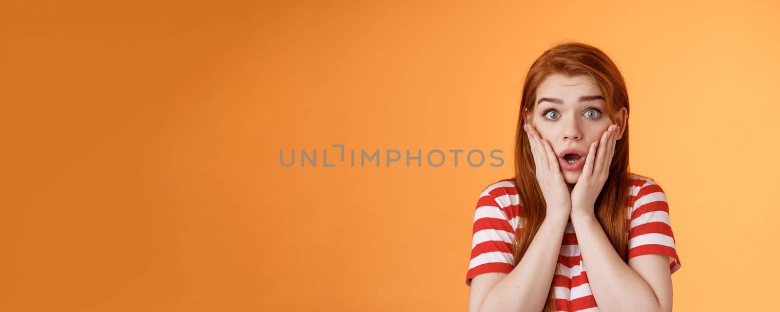 Close-up shocked speechless redhead woman, drop jaw gasping, touch cheeks embarrassed shook, look pity shame, stare camera astonished, surprised hear disturbing news, orange background by Benzoix