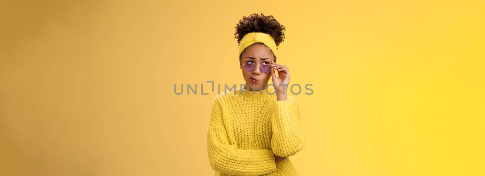Perplexed unsure stylish african-american female creative designer in headband sweater sunglasses smirking folding lips tube uncertain have doubts frowning look up thoughtful cannot decide.