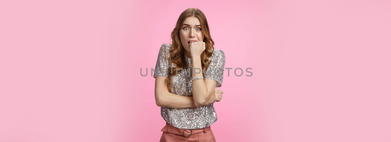 Worried insecure cute glamour caucasian woman biting fist nervously widen eyes scared bad consequences, frightened afraid parents find out, standing shocked stupor pink background.
