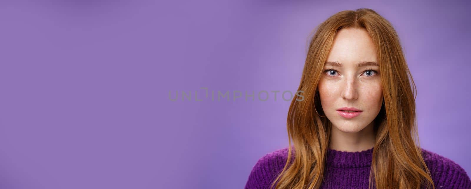 Headshot of sensual and attractive tender redhead female with freckles and pure skin looking at camera focused and sincere with slightly opened mouth, posing against purple background. People, expressions and emotions concept