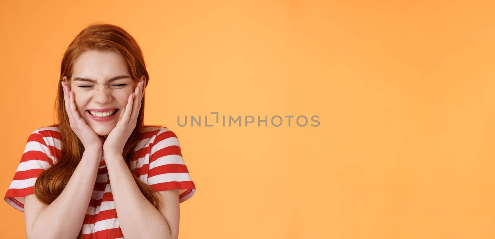 Close-up cheerful lucky excited smiling girl, cannot believe cheering hear excellent news, close eyes celebrating, touch cheeks blushing joy delight, rejoicing awesome situation, orange background.
