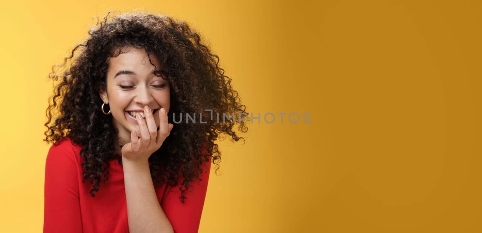 Girl laughing out loud cannot hold laugh as feeling amused hearing hilarious jokes covering mouth with palm as chuckling happily tilting forward with closed eyes, smiling over yellow wall. Emotions and body language concept