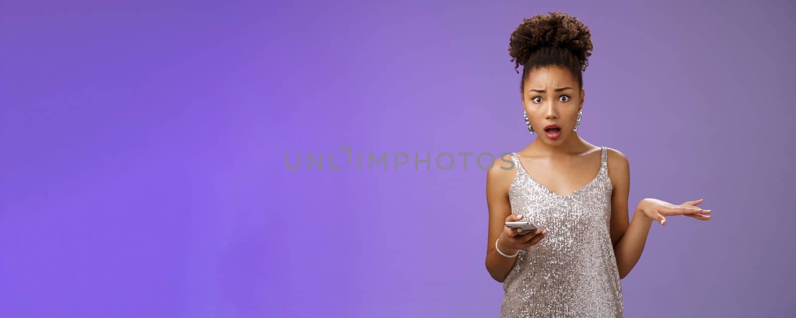 Concerned troubled arrogant silly glamour african american woman raise hand questioned holding smartphone insulted during phone call standing frustrated upset bothered blue background.
