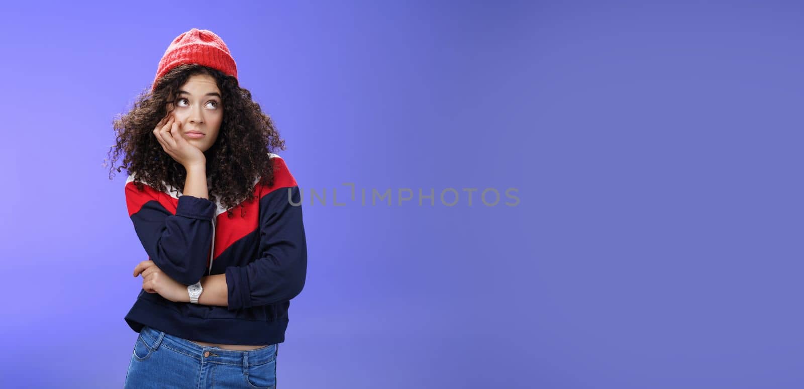 Portrait of frustrated and bored lonely girl with curly hair in winter hat holding hand across chest leaning head on palm, looking silly and gloomy at upper right corner, thinking feeling boredom by Benzoix
