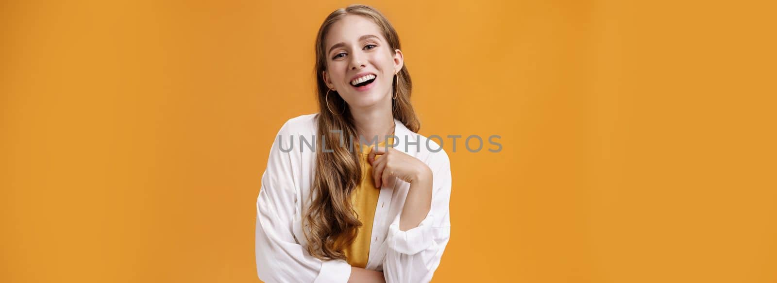 Stylish assertive and confident carefree woman dressing up on party laughing joyfully having fun and amusing talk standing pleased against orange background in white blouse over t-shirt by Benzoix