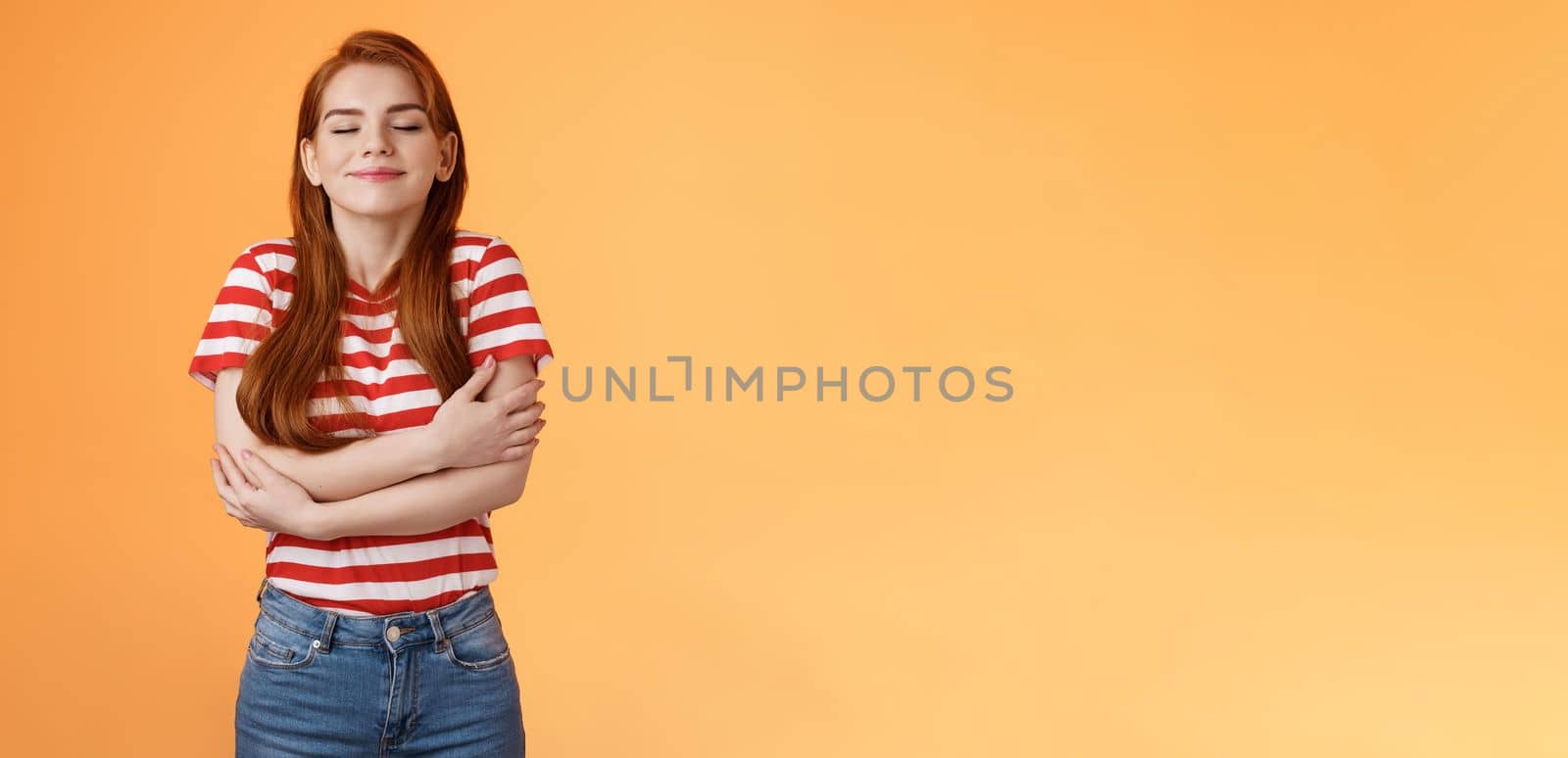 Tender lovely redhead modern woman embrace own body, feel happiness self-acceptance, smiling close eyes, cross arms, hugging herself dreamy, imaging something, daydreaming orange background.