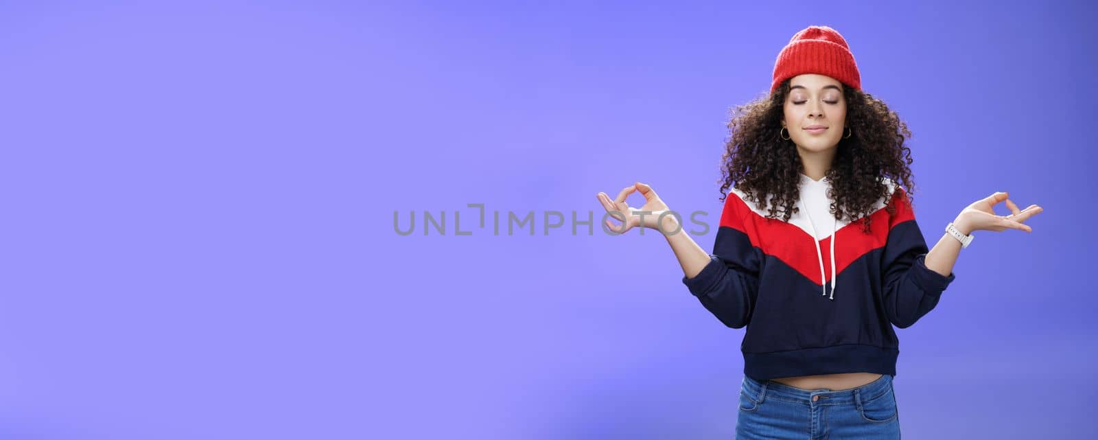 Waist-up shot of girl reaching nirvana feeling peaceful and calm holding hands sideways with mudra gesture close eyes, meditating releasing stress standing calm in lotus pose over blue background by Benzoix