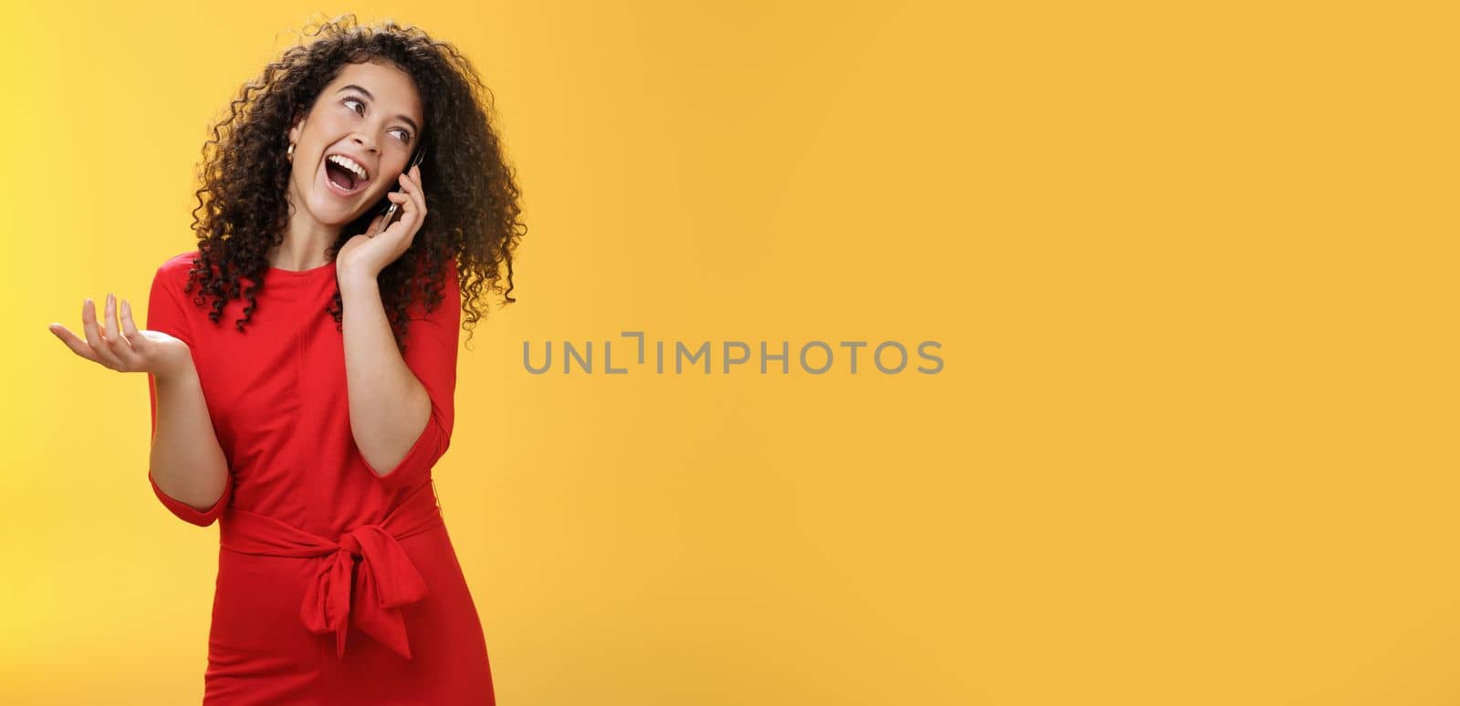 Lifestyle. Talkative glamour silly girl with curly hair having fun feeling carefree and happy taling on mobile phone turning away as laughing joyfully gesturing with hand holding smartphone pressed to ear.