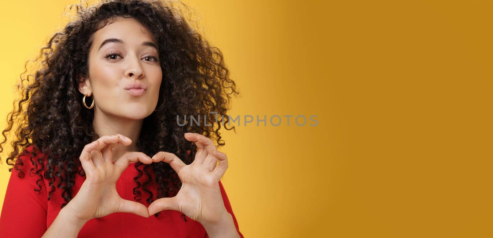 Close-up shot of romantic and tender young girlfriend with curly hair folding lips in kiss or mwah showing heart gesture, expressing love and romance, confessing in admiration or sympathy. Relationship, holidays and facial expressions concept