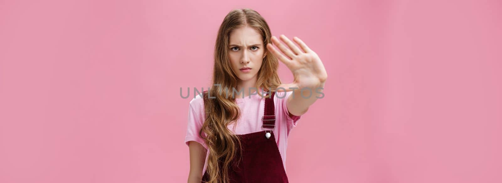 Woman protest against testing products on animals. Serious-looking confident young girl with long wavy hair frowning looking sctrict at camera pulling palm towards camera in prohibition and no gesture. Body language concept