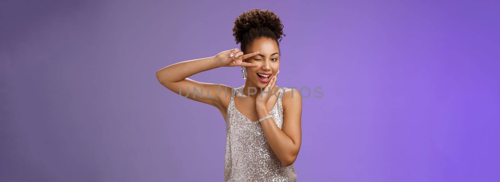 Sassy elegant confident african-american woman in stylish silver dress touch cheek show peace victory gesture feel lucky self-assured wear luxurious dress attend wealthy party, blue background.