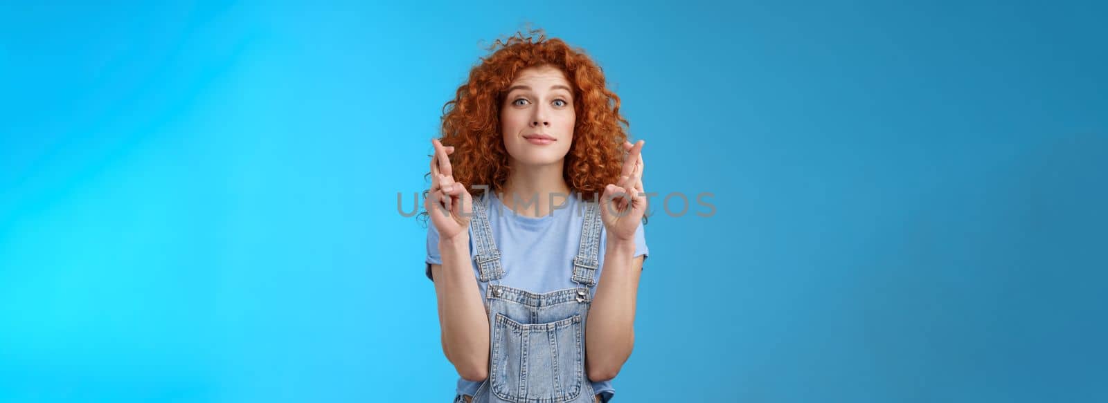 Lifestyle. Hopeful relaxed optimistic cute european redhead curly girl smiling faithfully awaiting good results believe wish come true cross fingers good luck grin anticipating important news dream fulfill.