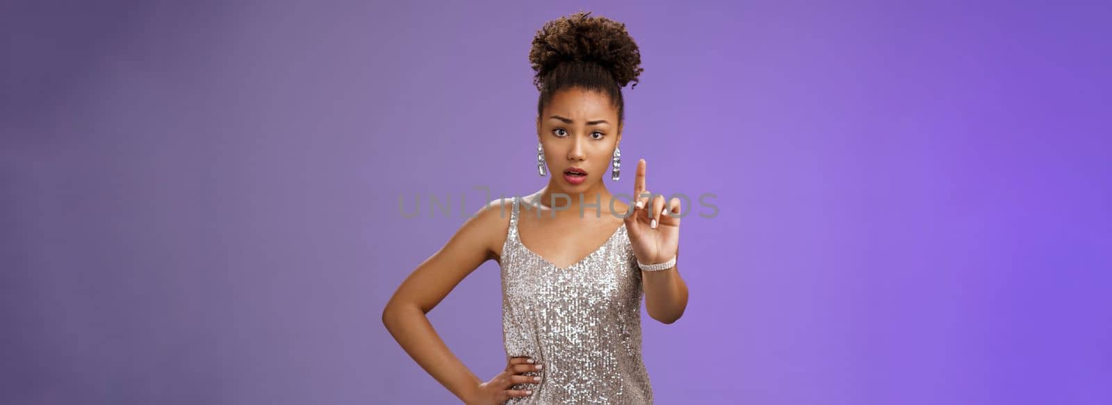 Concerned worried young african-american woman in trendy dress extend index finger nervously look camera shushing prohibiting tell anyone secret frowning afraid, saying taboo, blue background.