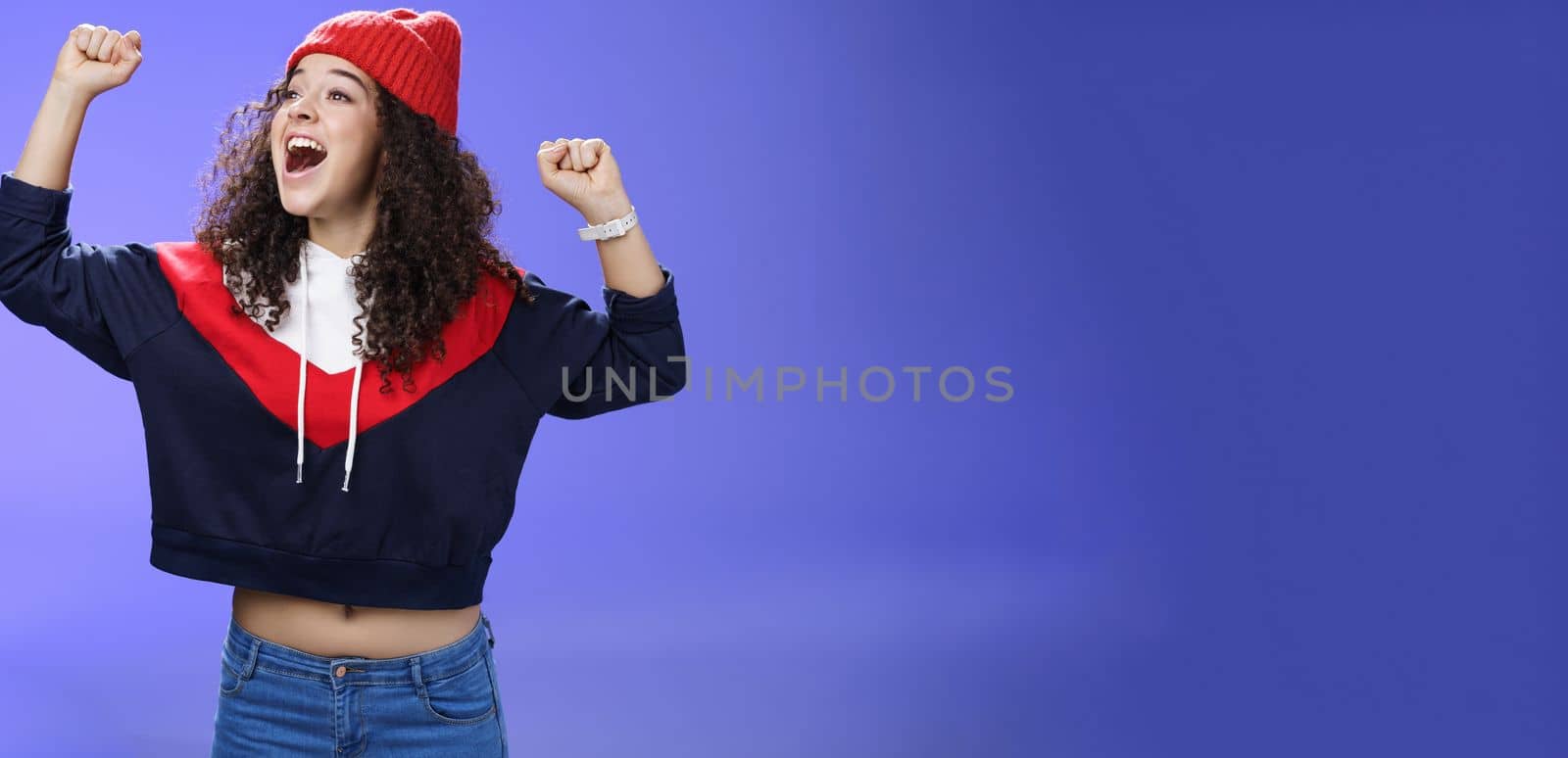 Happy playful and carefree woman yelling out loud tell world great news looking left amused and delighted as shouting positive words raising hands in triumph, cheering for team, wearing hat.