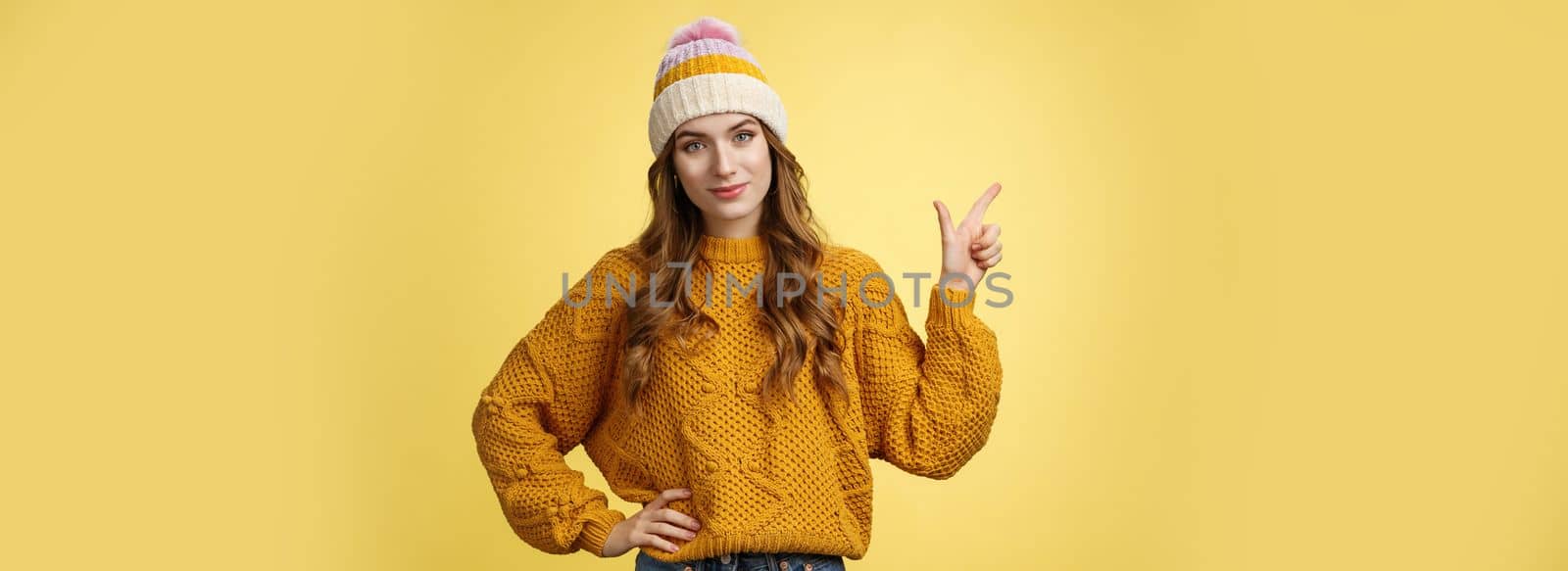 Confident good-looking young female friend telling you buy product immidietely pointing upper left corner smiling hold hand waist self-assured, employee help client pick best merch, yellow background.