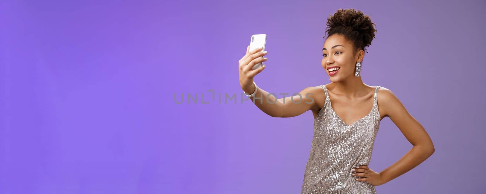 Confident glad attractive stylish millennial african-american woman in silver glittering dress taking selfie posing cute sassy hold hand waist extend arm record video message during night-out by Benzoix