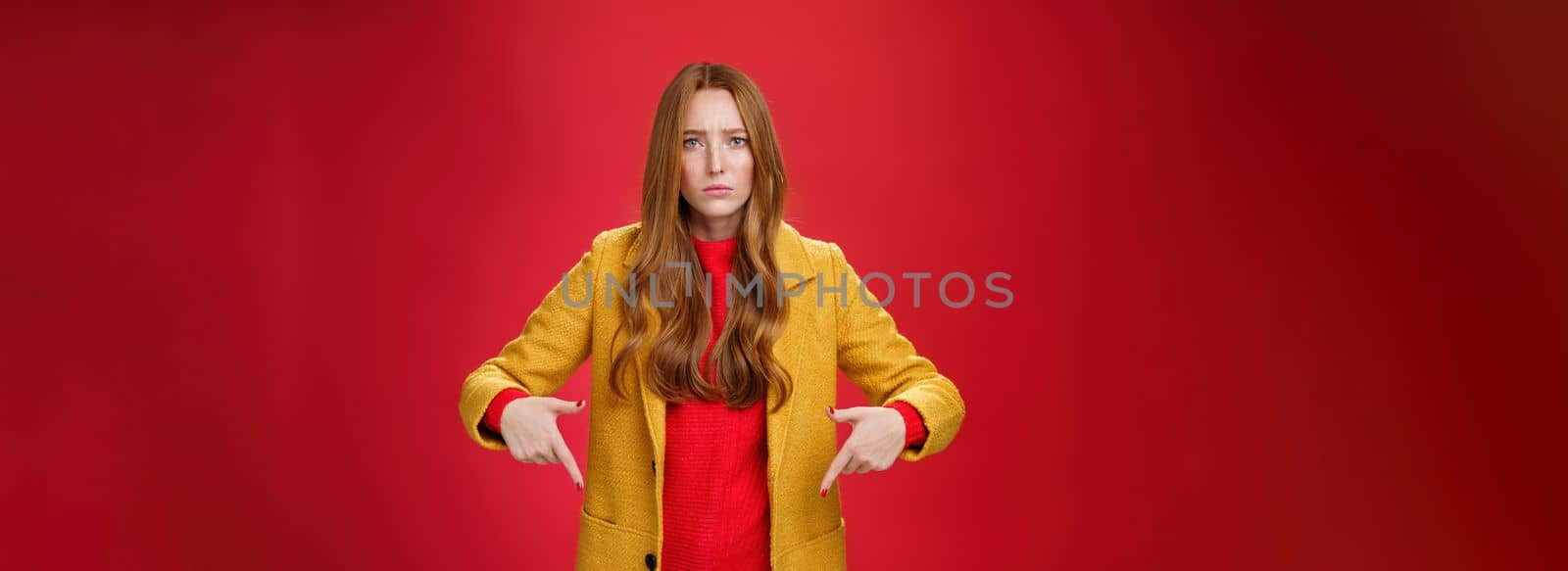 Portrait of sad and displeased moody girlfriend asking opinion with concerned upset expression pointing down looking focused and serious with unhappy face at camera over red background by Benzoix