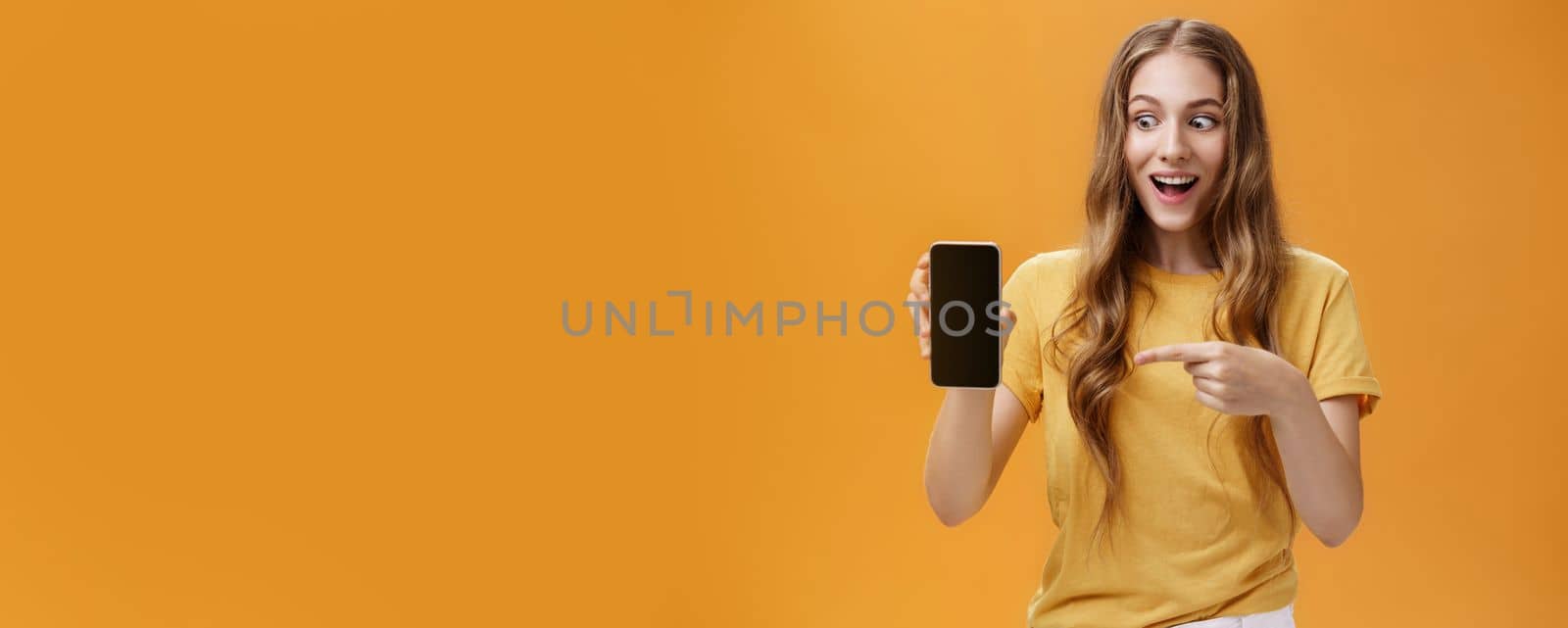 Lifestyle. Portrait of excited woman feeling amazed holding awesome new smartphone in hand pointing at cellphone screen popping eyes like crazy at device being charmed with cool technology product.