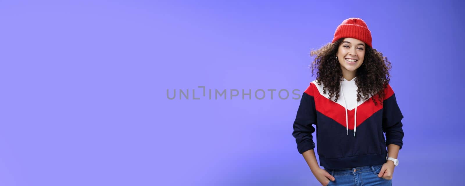 Girl invites join her team to srow snowballs. Portrait of friendly-looking carefree joyful woman with curly hair in red cute beanie and warm sweatshirt smiling joyfully getting ready for winter by Benzoix