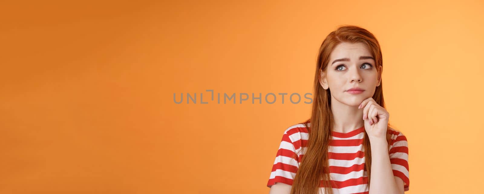 Close-up uneasy cute redhead female student facing tough troublesome decision, thinking intense, look upper left corner thoughtful touch chin, pondering between choices, frown focused.
