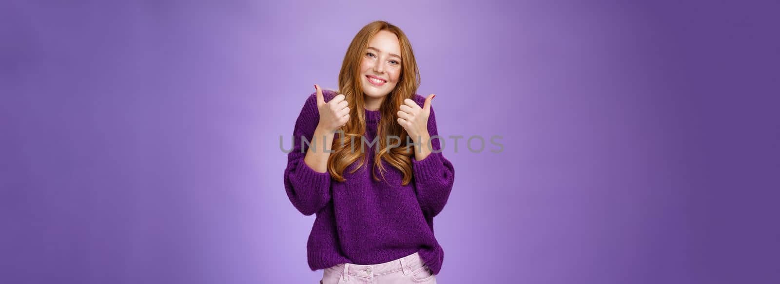 Portrait of happy and cute carefree ginger girl in 20s stooping as showing thumbs up in approval or like gesture smiling broadly supporting effort of friend with cheer, accepting idea.