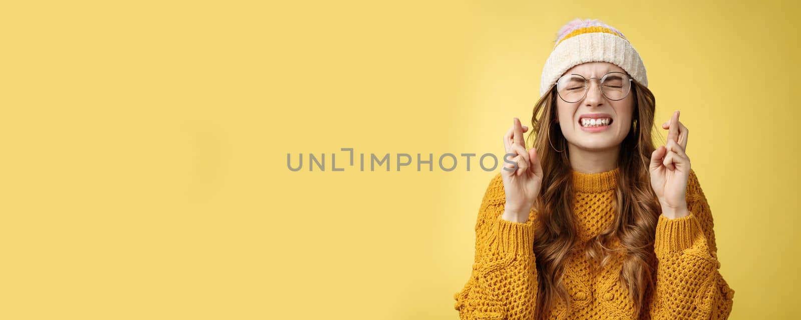 Close-up worried extremely nervous cute nerdy girl college student praying put effort dream come true clench teeth close eyes cross fingers good luck make wish standing supplicating yellow background by Benzoix