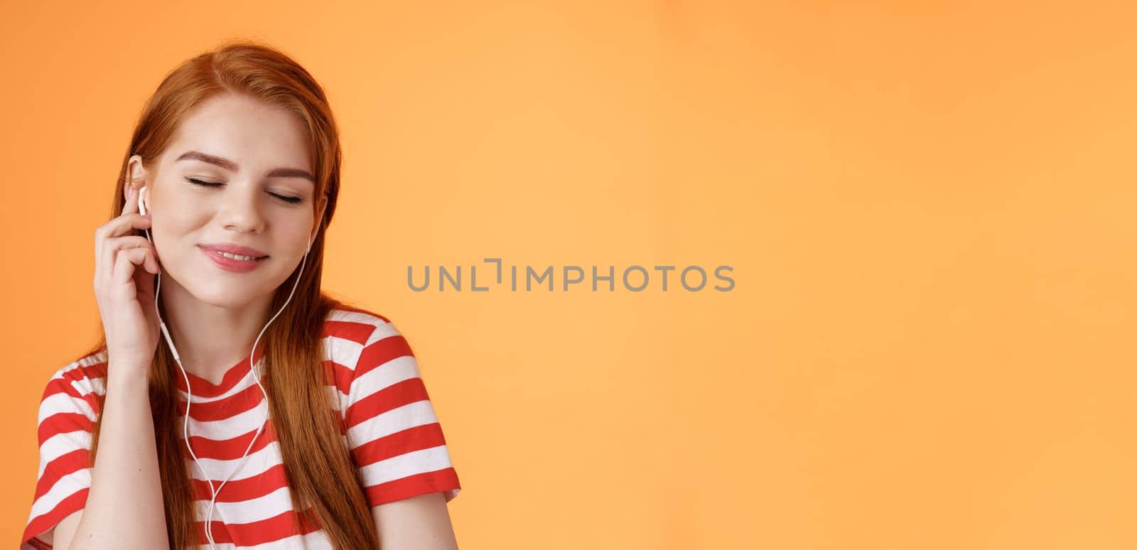 Lovely attractive redhead caucasian 20s woman listen music, close eyes tender smile, touch earphone ear, tilt head enjoyment and delight, hear nice beats, favorite music track, orange background by Benzoix