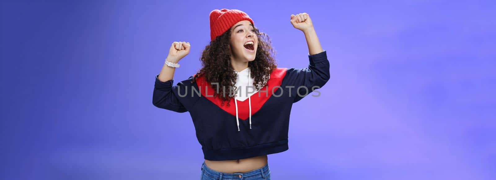 Happy playful and carefree woman yelling out loud tell world great news looking left amused and delighted as shouting positive words raising hands in triumph, cheering for team, wearing hat.